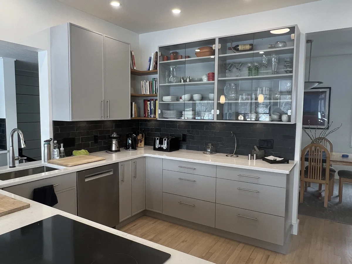 Kitchen with gray cabinets and glass-front shelving by DeFaria Construction