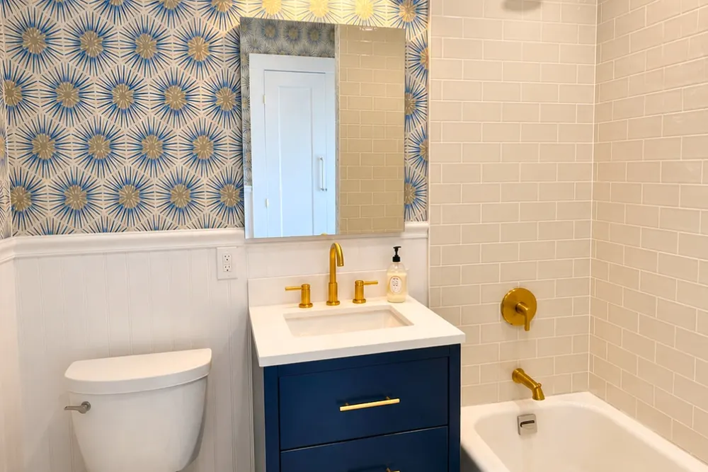 Bathroom with patterned wallpaper, navy vanity and brass fixtures by DeFaria Construction