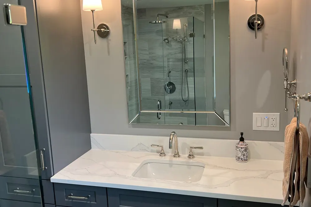 Primary bathroom vanity with marble top, framed mirror and wall sconces in Westford, MA, by DeFaria Construction