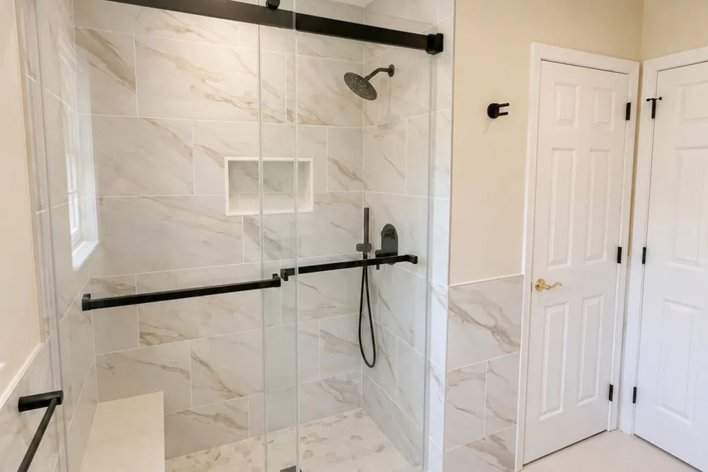 Walk-in shower with marble-look tile, niche and black sliding glass door by DeFaria Construction
