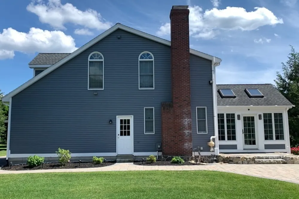 Side of a colonial home with new blue siding, white trim and brick chimney, Westford MA