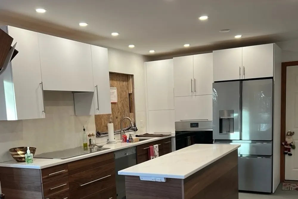 Modern kitchen with white upper cabinets, wood tone base cabinets and island in Pepperell, MA, by DeFaria Construction
