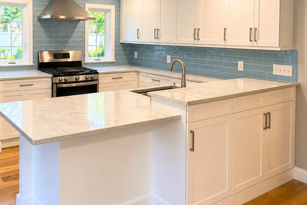 White shaker kitchen with quartz island and glass tile backsplash by DeFaria Construction