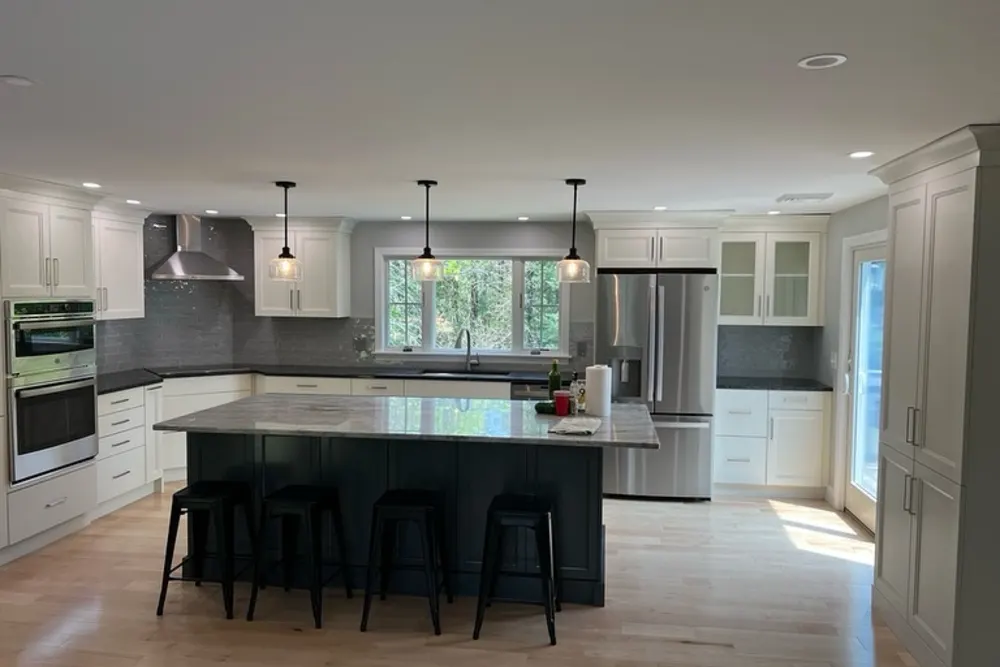 Open kitchen with white cabinets, dark island and pendant lights in Pepperell, MA, by DeFaria Construction